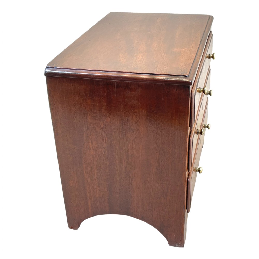 A small Georgian mahogany miniature chest featuring three drawers with brass knob handles, diamond-shaped escutcheons, and a shaped apron. View II