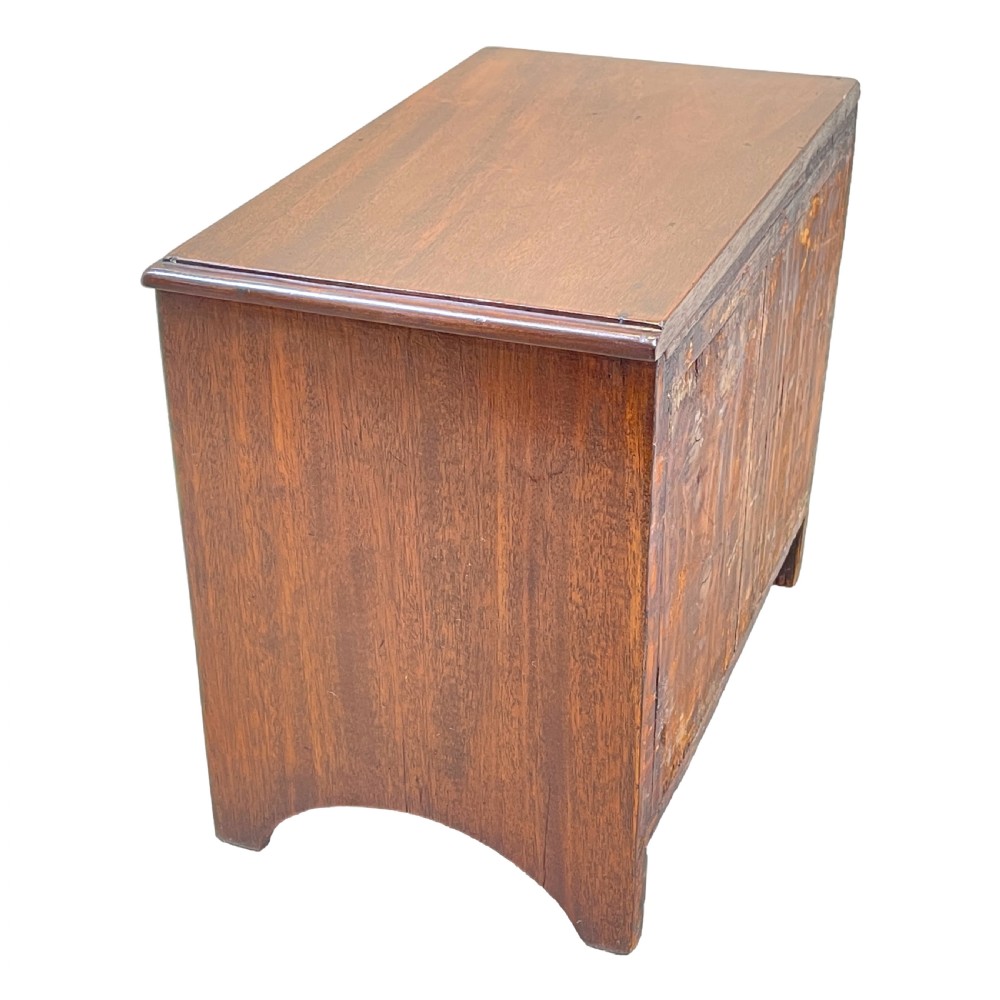 A small Georgian mahogany miniature chest featuring three drawers with brass knob handles, diamond-shaped escutcheons, and a shaped apron. View VI