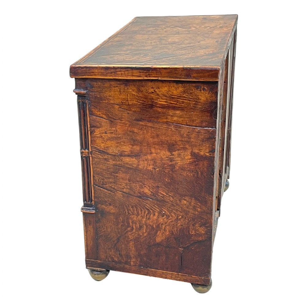 A Regency era miniature chest of drawers crafted from burr oak with geometric inlay, brass knobs, reeded pilasters, and small turned ball feet. View III