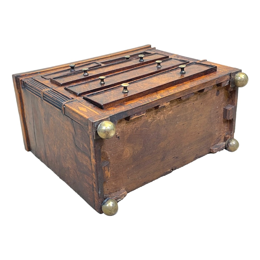 A Regency era miniature chest of drawers crafted from burr oak with geometric inlay, brass knobs, reeded pilasters, and small turned ball feet. View X