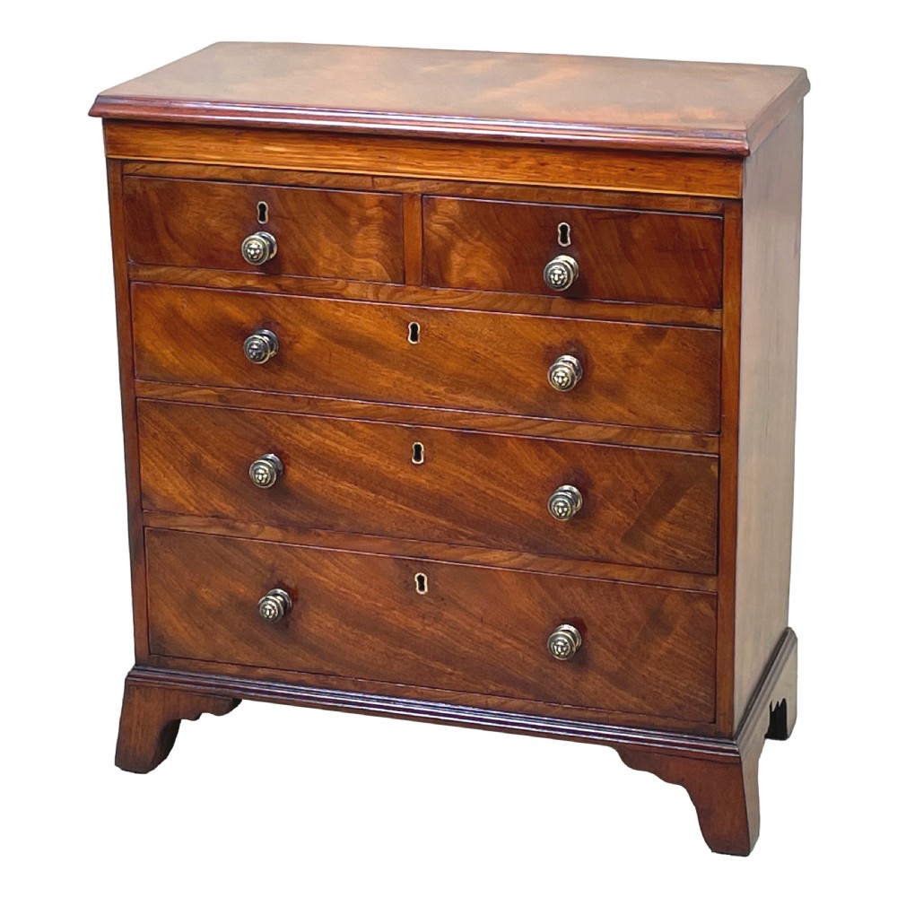 A Georgian miniature chest of drawers in flame mahogany featuring two short drawers over three long drawers with turned knobs and bracket feet.