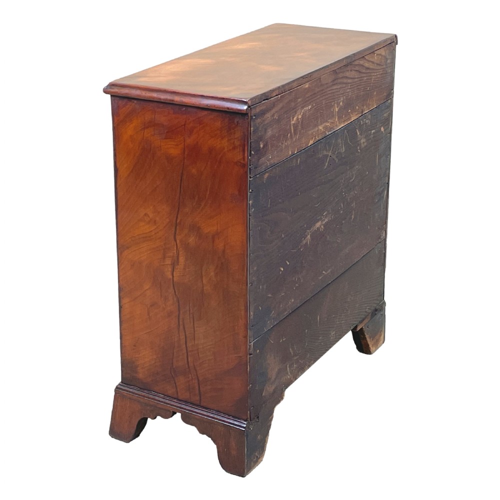 A Georgian miniature chest of drawers in flame mahogany featuring two short drawers over three long drawers with turned knobs and bracket feet. View III