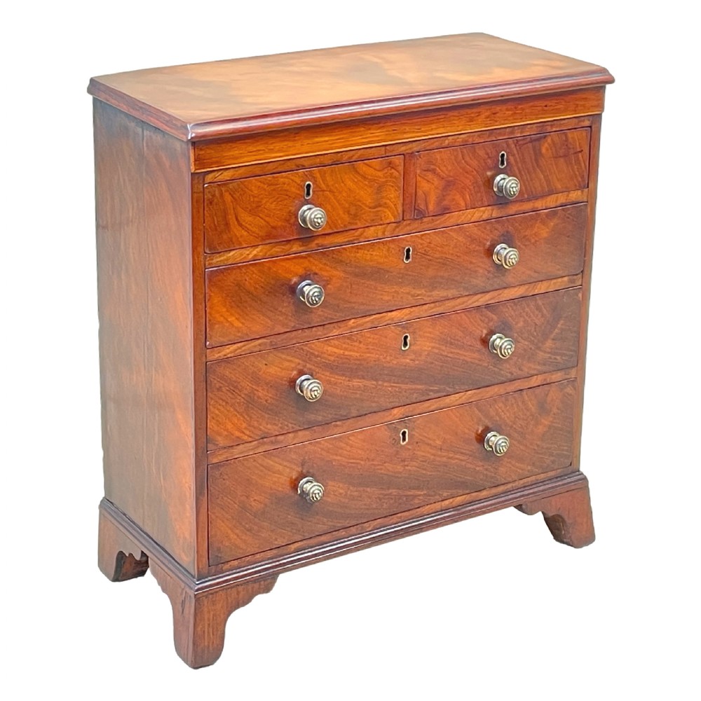 A Georgian miniature chest of drawers in flame mahogany featuring two short drawers over three long drawers with turned knobs and bracket feet. View IV