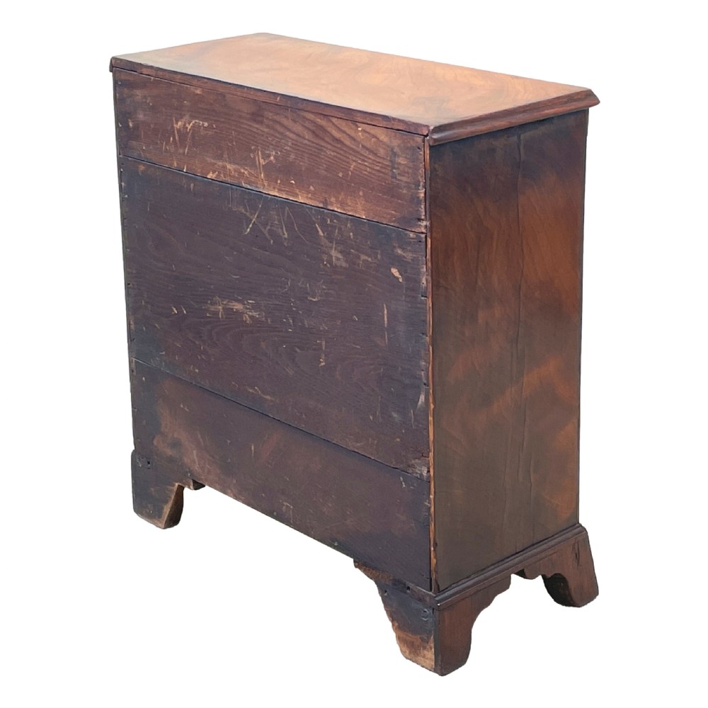 A Georgian miniature chest of drawers in flame mahogany featuring two short drawers over three long drawers with turned knobs and bracket feet. View VI