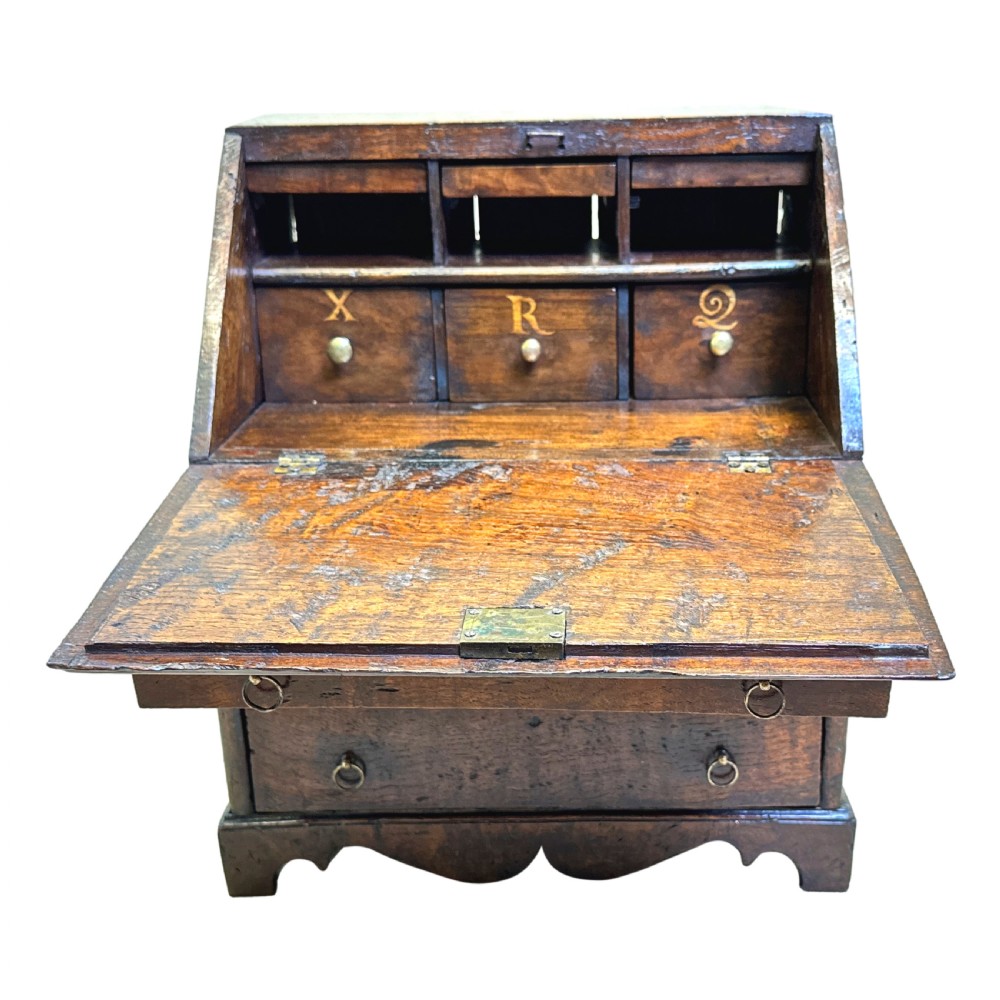 An 18th-century Georgian tabletop bureau made of dark warm elm wood, featuring a sloped writing flap above three drawers with brass ring pulls and a scalloped base. View III