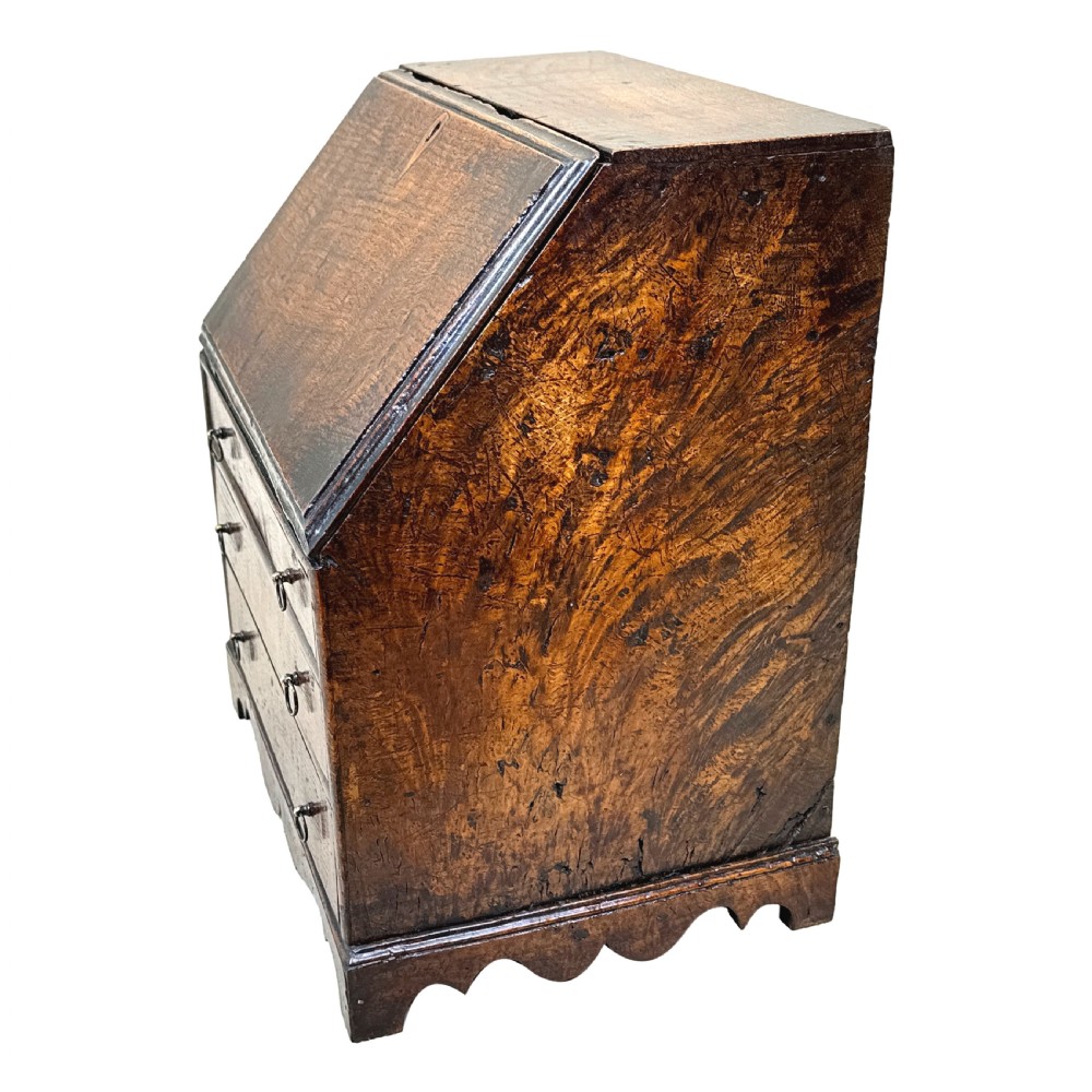 An 18th-century Georgian tabletop bureau made of dark warm elm wood, featuring a sloped writing flap above three drawers with brass ring pulls and a scalloped base. View IV