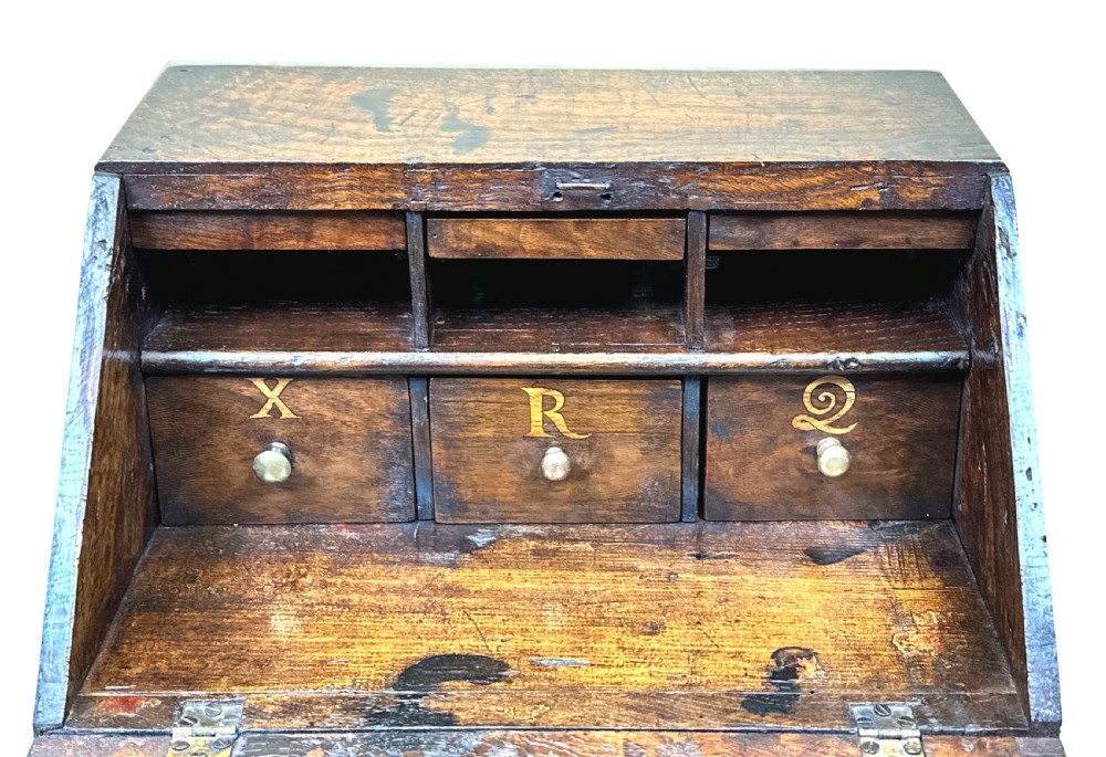 An 18th-century Georgian tabletop bureau made of dark warm elm wood, featuring a sloped writing flap above three drawers with brass ring pulls and a scalloped base. View VII