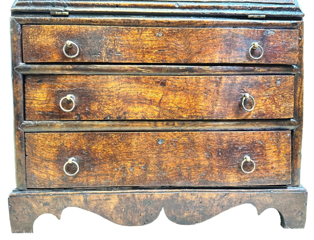 An 18th-century Georgian tabletop bureau made of dark warm elm wood, featuring a sloped writing flap above three drawers with brass ring pulls and a scalloped base. View VIII