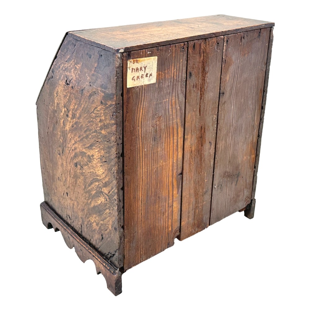 An 18th-century Georgian tabletop bureau made of dark warm elm wood, featuring a sloped writing flap above three drawers with brass ring pulls and a scalloped base. View IX