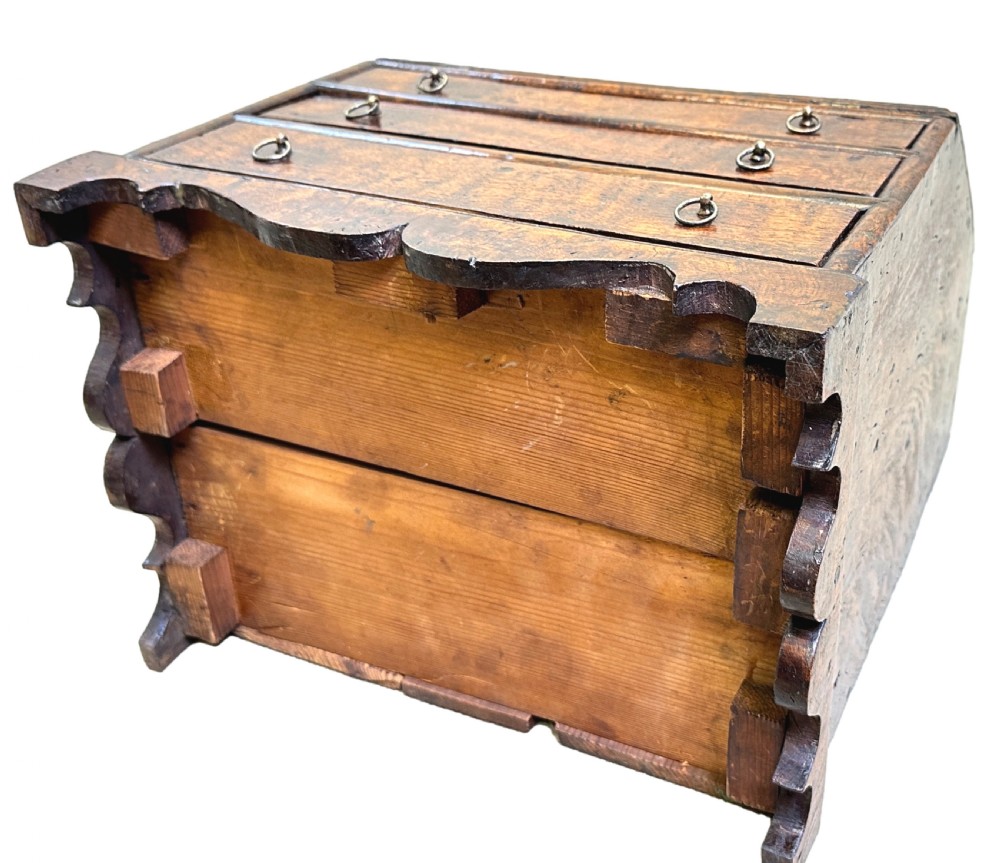 An 18th-century Georgian tabletop bureau made of dark warm elm wood, featuring a sloped writing flap above three drawers with brass ring pulls and a scalloped base. View X