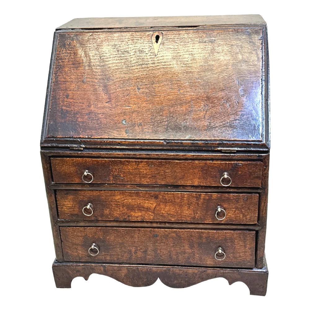 An 18th-century Georgian tabletop bureau made of dark warm elm wood, featuring a sloped writing flap above three drawers with brass ring pulls and a scalloped base. View XI