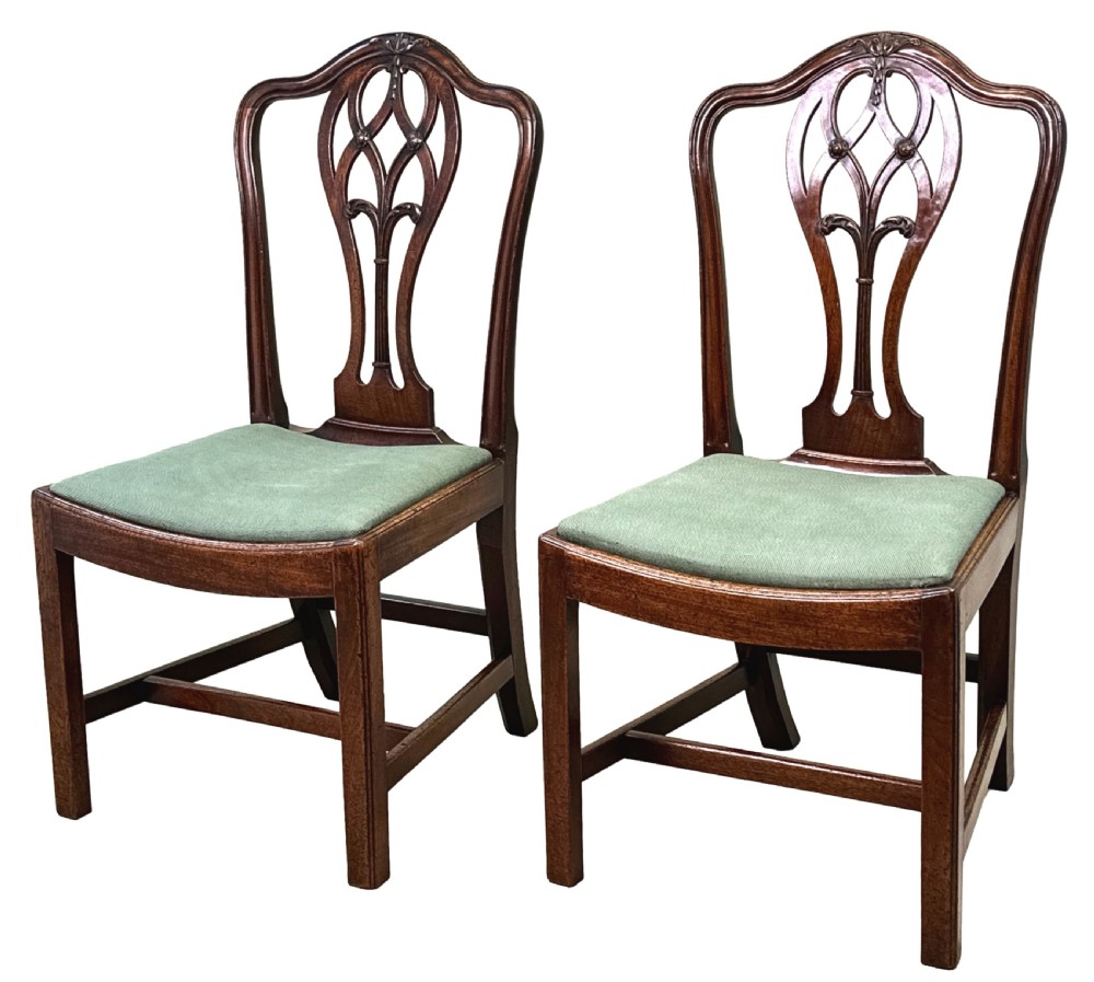 A pair of 18th-century Georgian mahogany side chairs featuring pierced back splats, serpentine top rails, and light green upholstered drop-in seats.