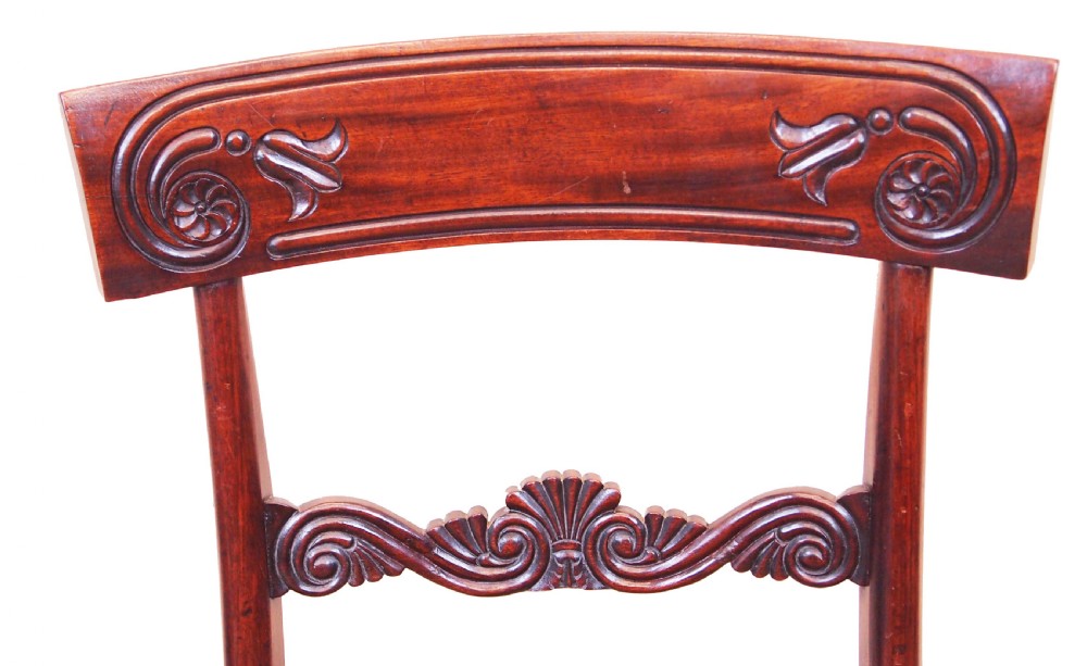 A set of eight Regency period mahogany dining chairs, including two carver armchairs and six side chairs, featuring carved bar backs and upholstered seats. View V