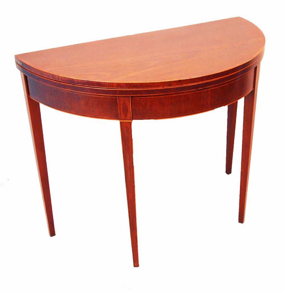 A Georgian mahogany demilune tea table featuring a semicircular fold-over top, inlaid apron, and four square tapered legs.