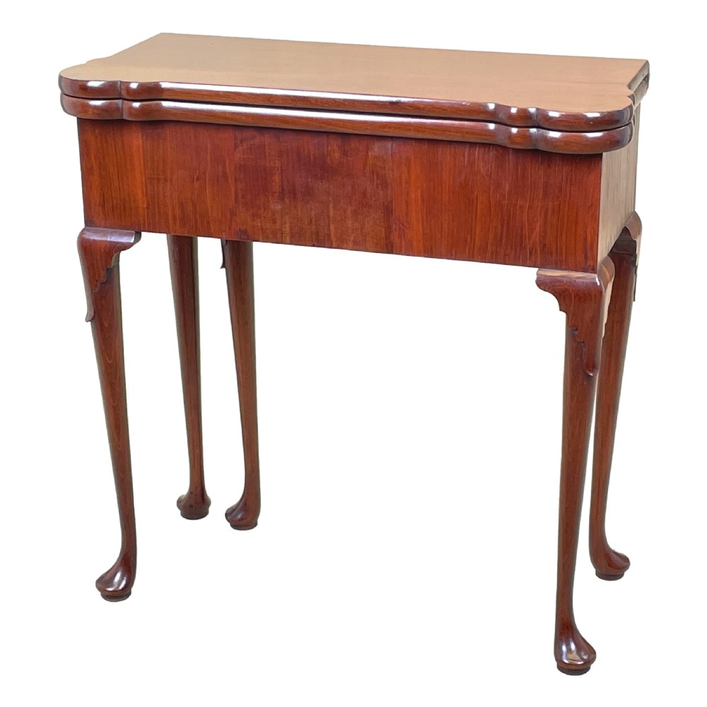 An 18th-century walnut tea table featuring a fold-over rectangular top with shaped corners, elevated on slender cabriole legs with pad feet.