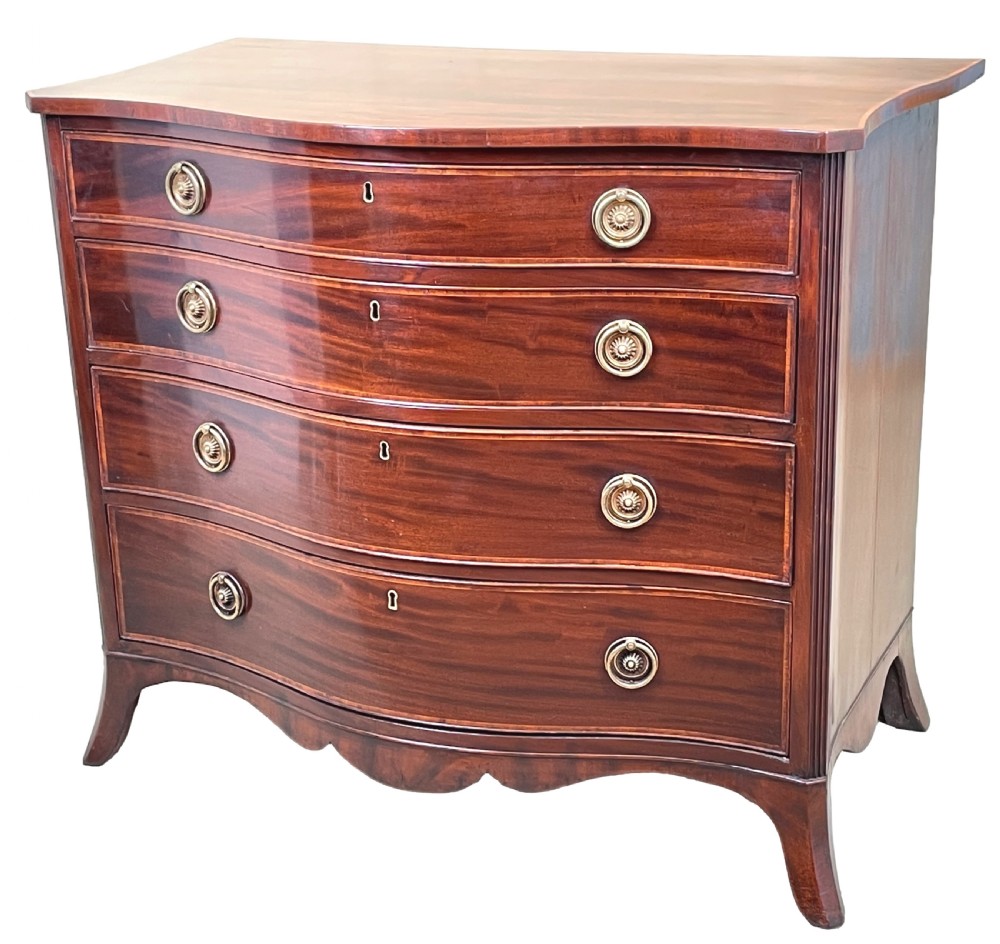 A Georgian style mahogany chest of drawers featuring a serpentine front, four graduated drawers with brass ring handles, and bracket feet.