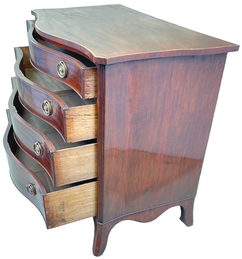 A Georgian style mahogany chest of drawers featuring a serpentine front, four graduated drawers with brass ring handles, and bracket feet. View X