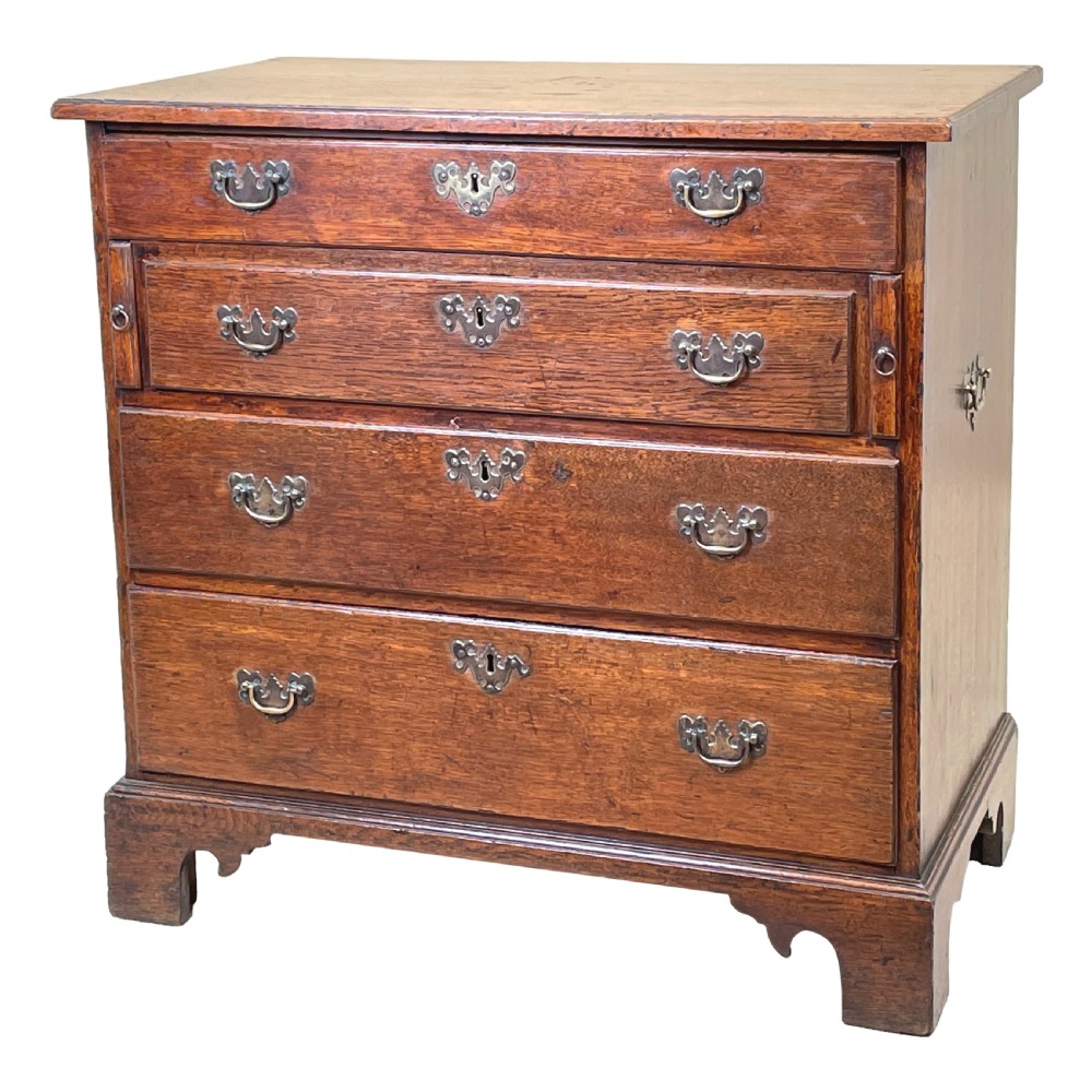 An eighteenth-century oak bachelors chest featuring four drawers with brass drop handles, escutcheons, a pull-out brushing slide, and bracket feet.