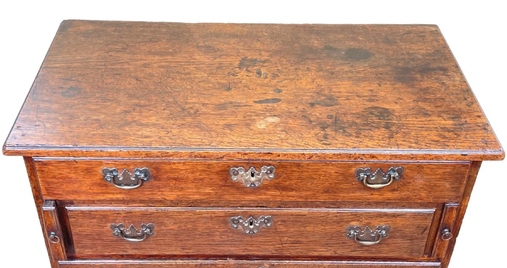 An eighteenth-century oak bachelors chest featuring four drawers with brass drop handles, escutcheons, a pull-out brushing slide, and bracket feet. View III