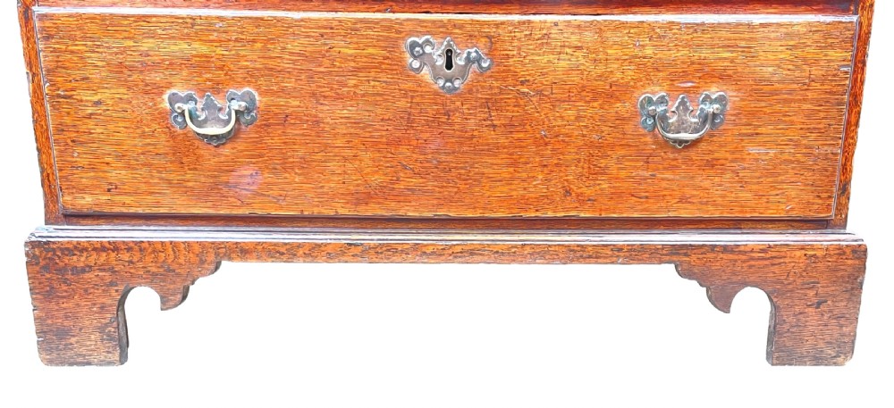 An eighteenth-century oak bachelors chest featuring four drawers with brass drop handles, escutcheons, a pull-out brushing slide, and bracket feet. View VIII