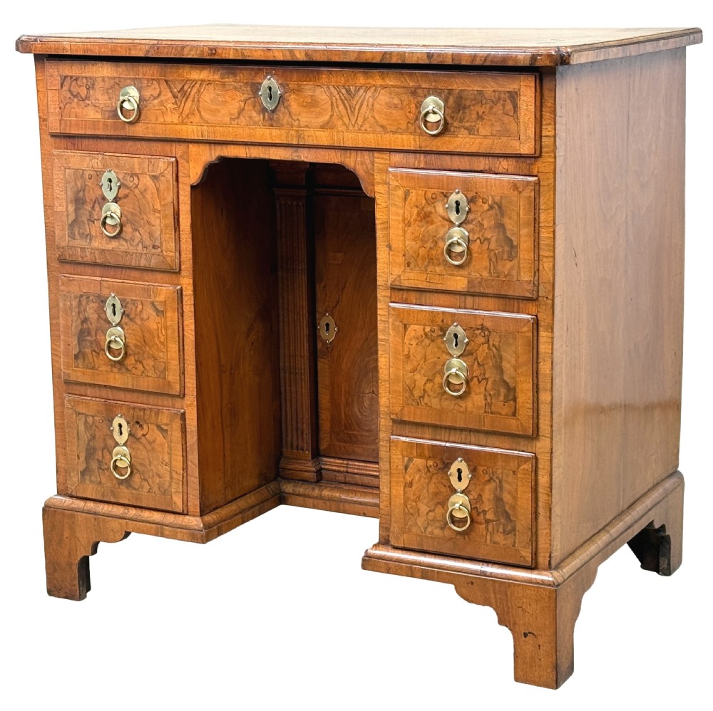 An 18th-century Georgian walnut kneehole desk featuring figured veneer drawer fronts, brass drop handles, and bracket feet.