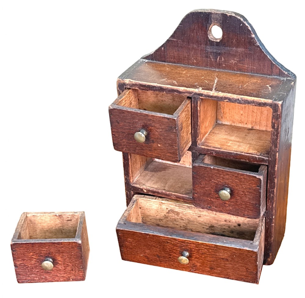 A 19th-century dark brown oak and pine wall-hanging spice box featuring five small drawers with brass knobs and an arched backboard with a central mounting hole. View II