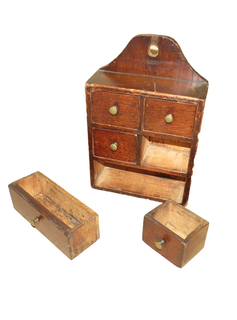 A 19th-century dark brown oak and pine wall-hanging spice box featuring five small drawers with brass knobs and an arched backboard with a central mounting hole. View VI