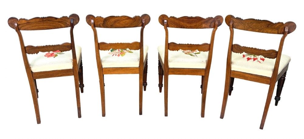 A set of ten Regency rosewood dining chairs featuring carved crest rails, scrolled mid-bars, turned front legs, and cream embroidered needlepoint seats. View V