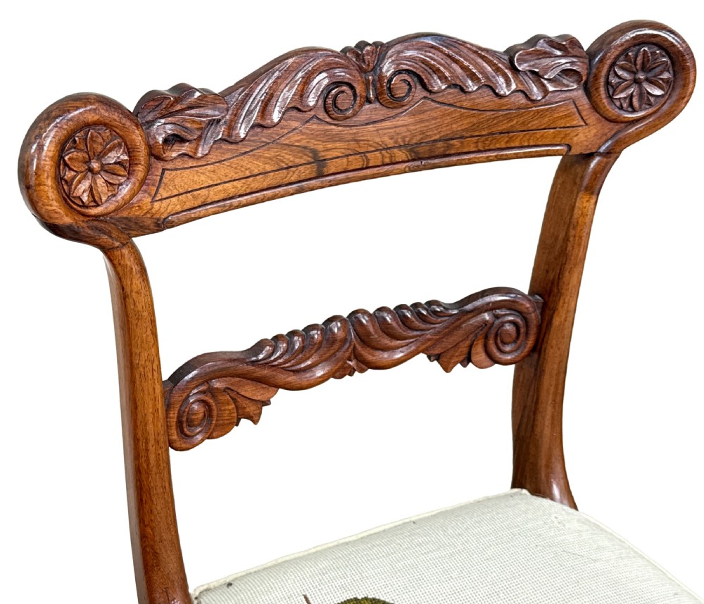 A set of ten Regency rosewood dining chairs featuring carved crest rails, scrolled mid-bars, turned front legs, and cream embroidered needlepoint seats. View VII