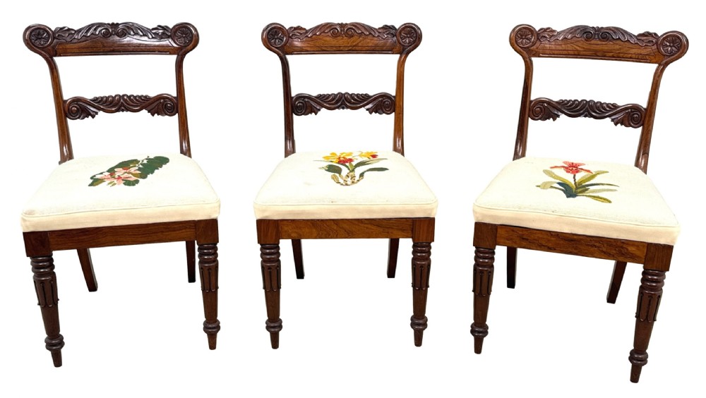 A set of ten Regency rosewood dining chairs featuring carved crest rails, scrolled mid-bars, turned front legs, and cream embroidered needlepoint seats. View VIII