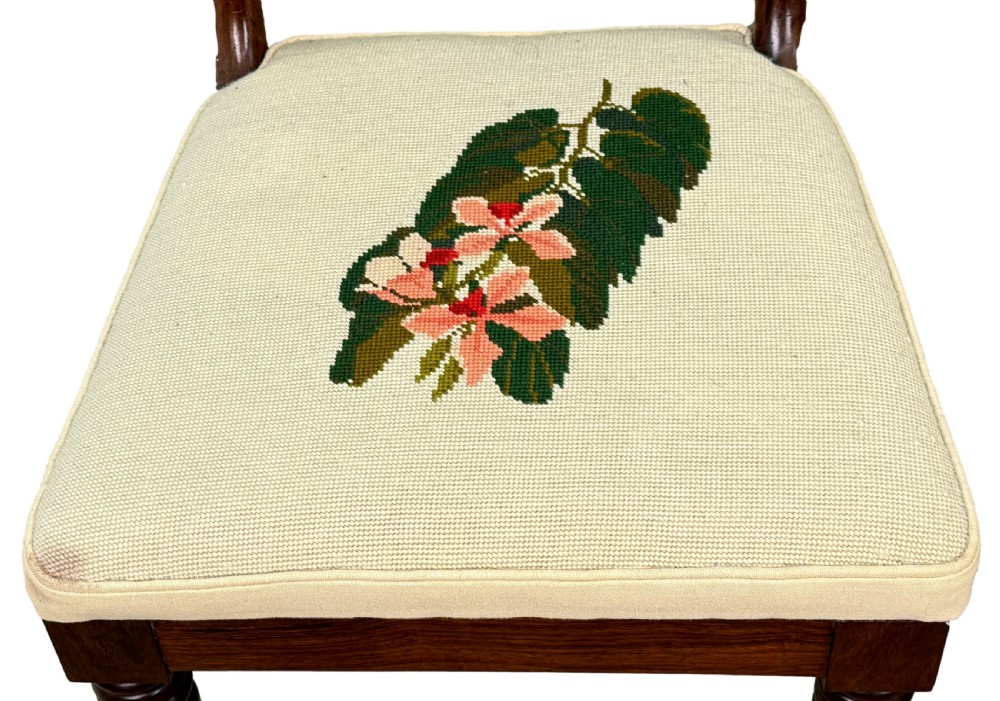 A set of ten Regency rosewood dining chairs featuring carved crest rails, scrolled mid-bars, turned front legs, and cream embroidered needlepoint seats. View IX