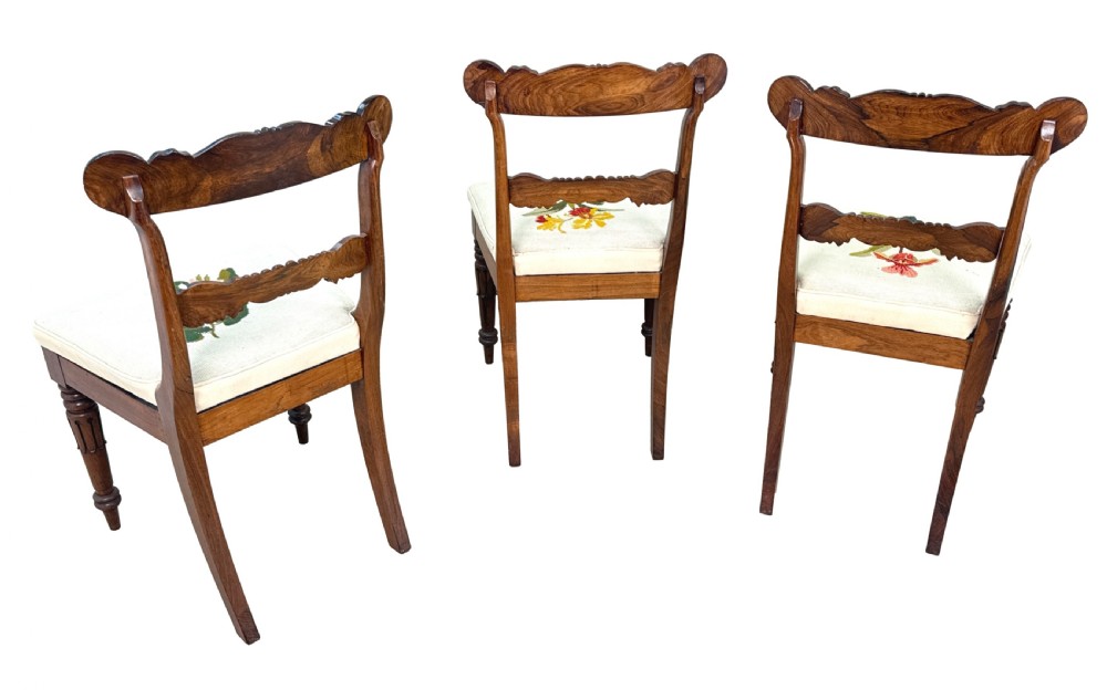 A set of ten Regency rosewood dining chairs featuring carved crest rails, scrolled mid-bars, turned front legs, and cream embroidered needlepoint seats. View XII
