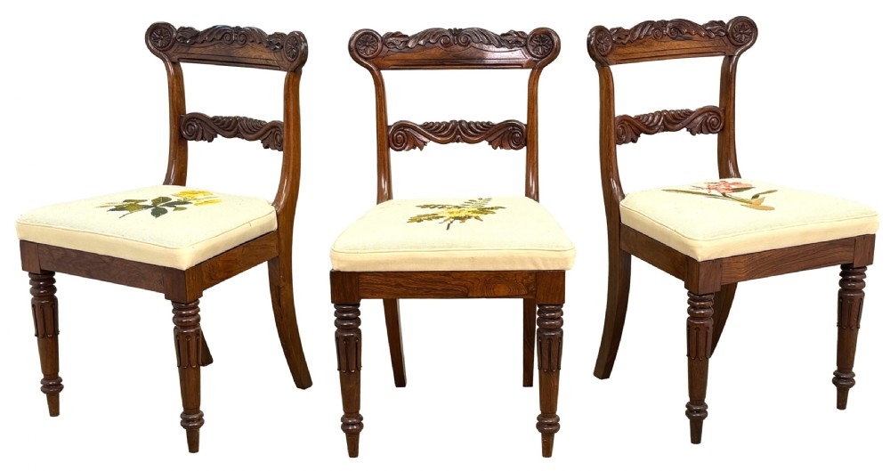 A set of ten Regency rosewood dining chairs featuring carved crest rails, scrolled mid-bars, turned front legs, and cream embroidered needlepoint seats. View XV
