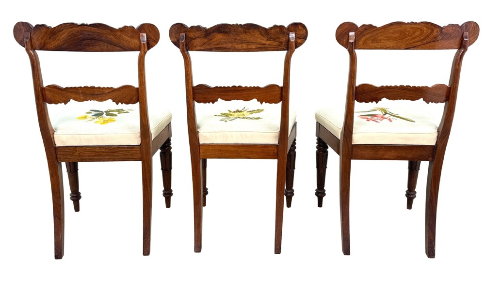 A set of ten Regency rosewood dining chairs featuring carved crest rails, scrolled mid-bars, turned front legs, and cream embroidered needlepoint seats. View XIX