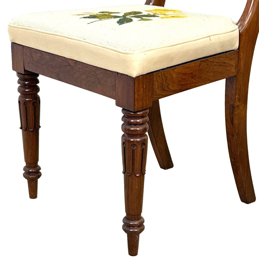A set of ten Regency rosewood dining chairs featuring carved crest rails, scrolled mid-bars, turned front legs, and cream embroidered needlepoint seats. View XXI