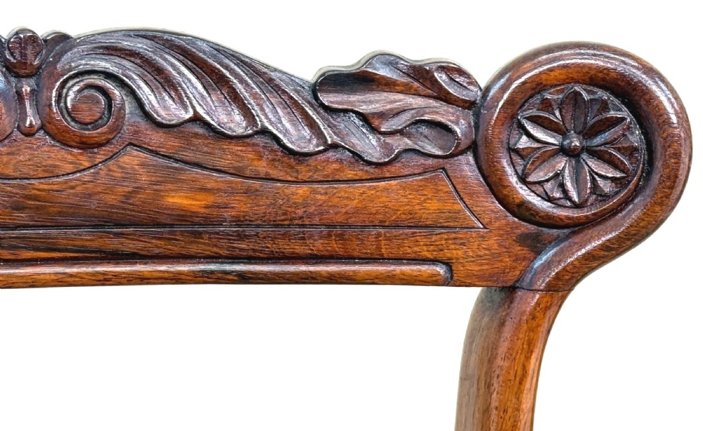 A set of ten Regency rosewood dining chairs featuring carved crest rails, scrolled mid-bars, turned front legs, and cream embroidered needlepoint seats. View XXII