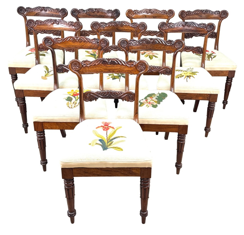 A set of ten Regency rosewood dining chairs featuring carved crest rails, scrolled mid-bars, turned front legs, and cream embroidered needlepoint seats. View XXIII