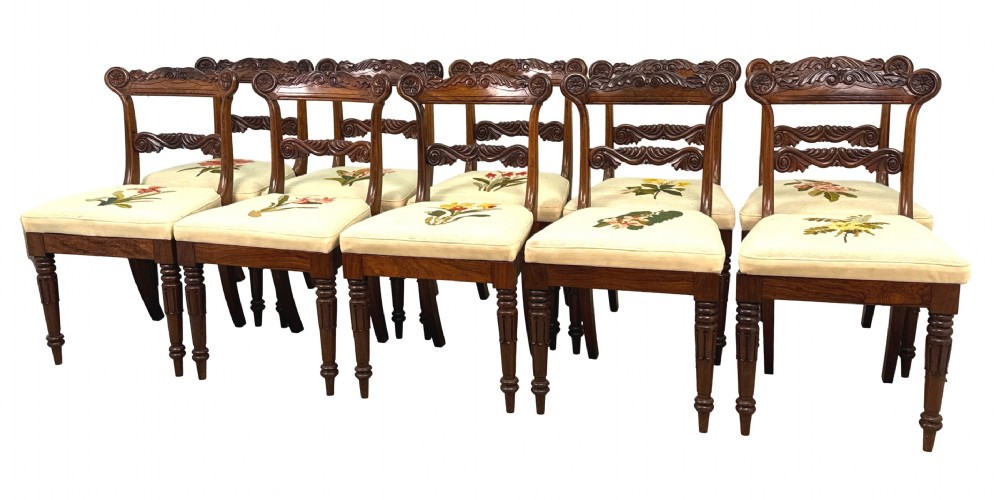 A set of ten Regency rosewood dining chairs featuring carved crest rails, scrolled mid-bars, turned front legs, and cream embroidered needlepoint seats.