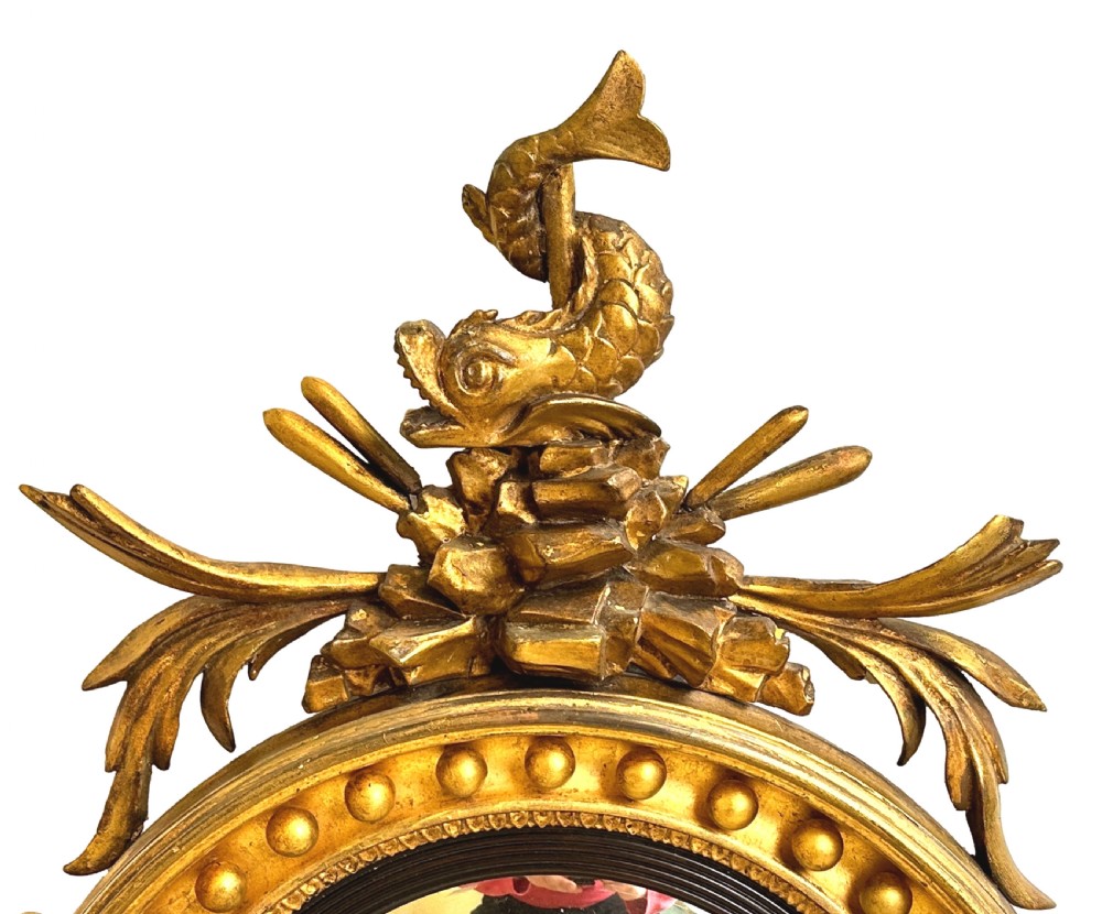 A circular Regency giltwood convex mirror featuring a carved dolphin crest, ball moulding, ebonised inner rim, lower acanthus apron, and twin candle sconces. View IV