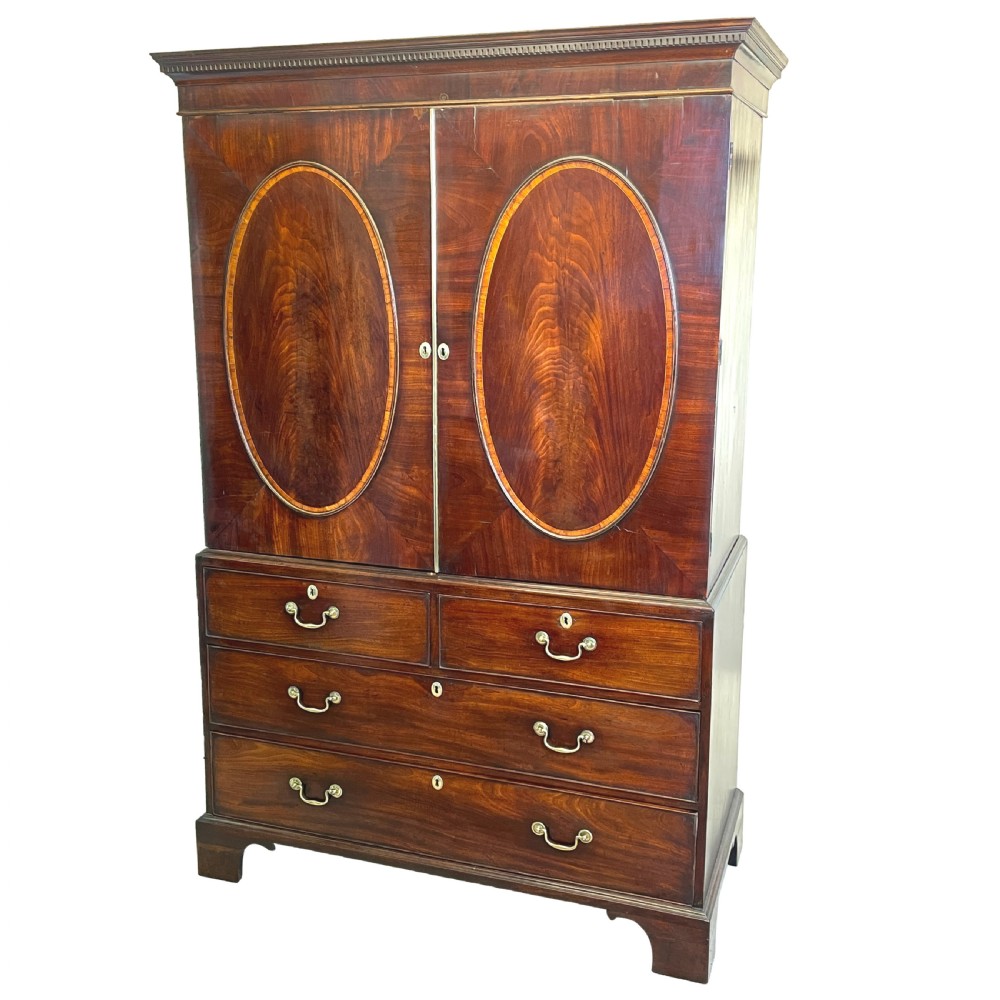 A Georgian mahogany linen press featuring an upper cabinet with oval flame mahogany veneered panels above a chest with four drawers.