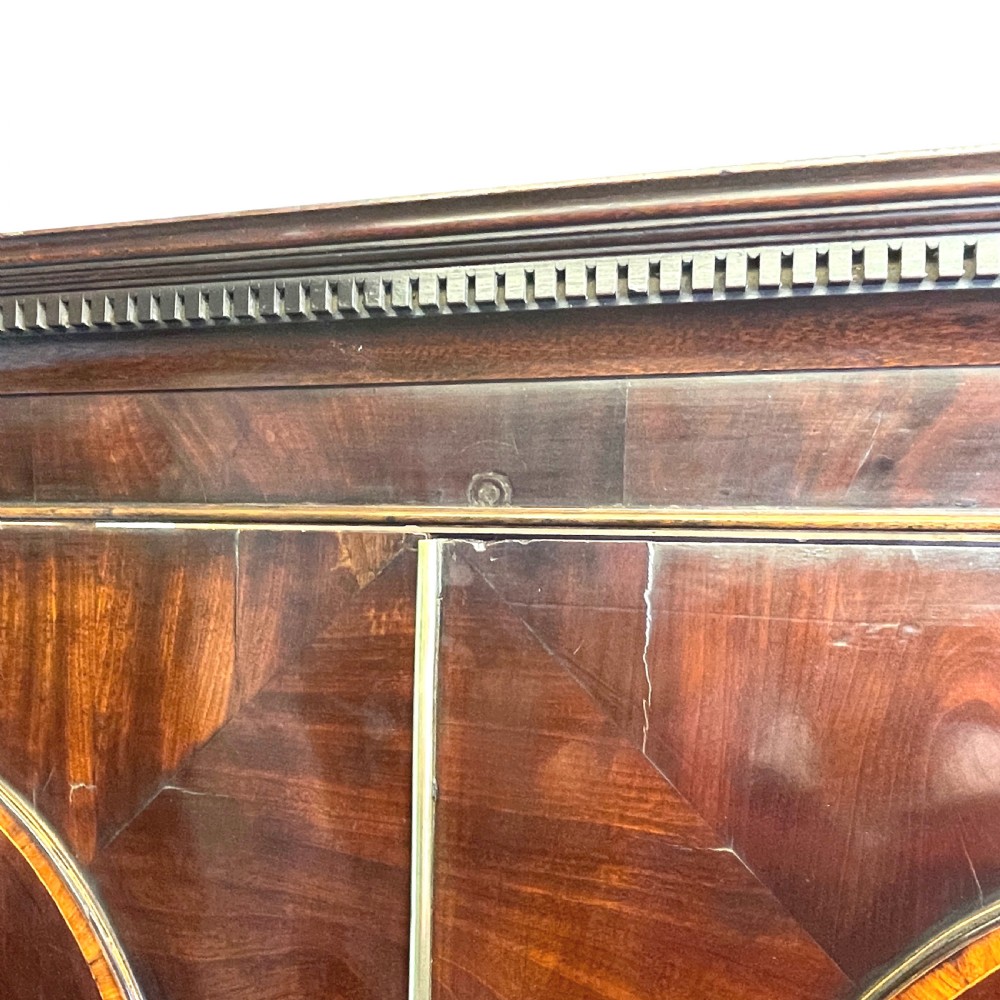 A Georgian mahogany linen press featuring an upper cabinet with oval flame mahogany veneered panels above a chest with four drawers. View II