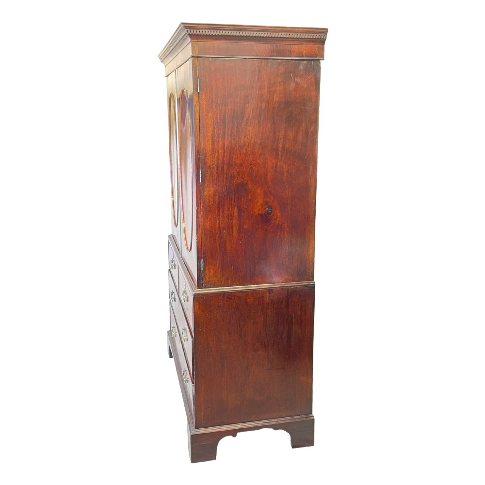 A Georgian mahogany linen press featuring an upper cabinet with oval flame mahogany veneered panels above a chest with four drawers. View V