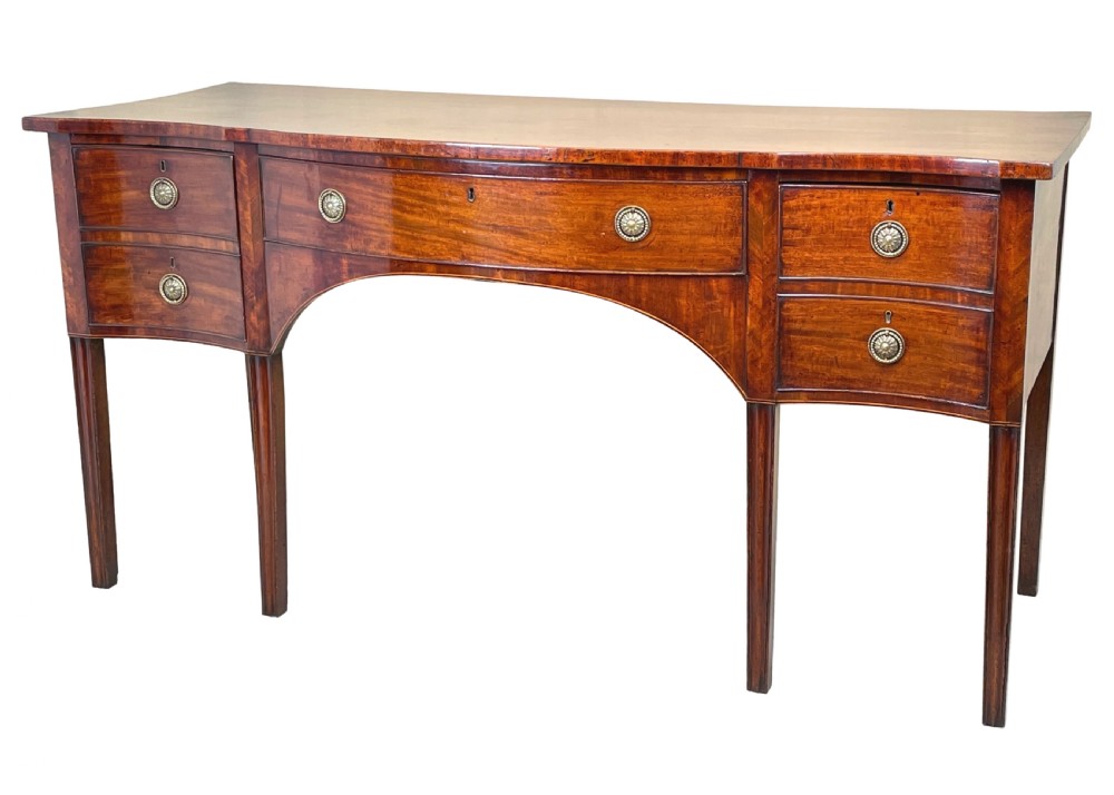 A Georgian mahogany serpentine-front sideboard featuring a polished wood top, central arched drawer, flanking drawers with brass rosette handles, and tapered square legs.