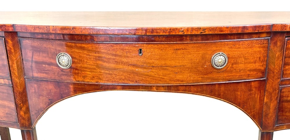 A Georgian mahogany serpentine-front sideboard featuring a polished wood top, central arched drawer, flanking drawers with brass rosette handles, and tapered square legs. View II