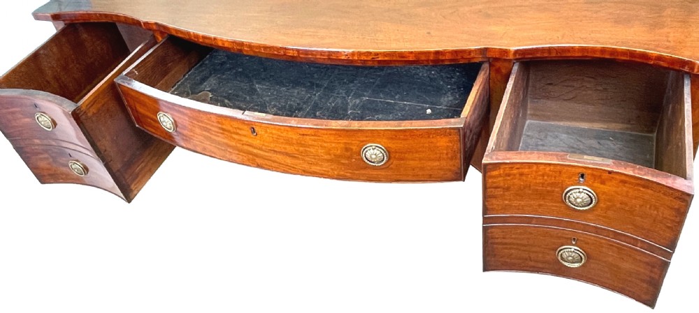 A Georgian mahogany serpentine-front sideboard featuring a polished wood top, central arched drawer, flanking drawers with brass rosette handles, and tapered square legs. View III