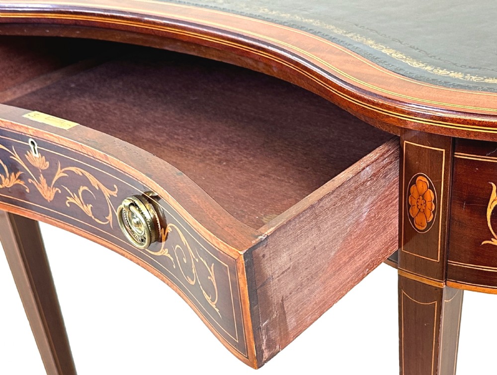 A nineteenth-century mahogany kidney-shaped writing table featuring foliate marquetry, a dark leather insert, and square tapered legs with brass castors. View VI