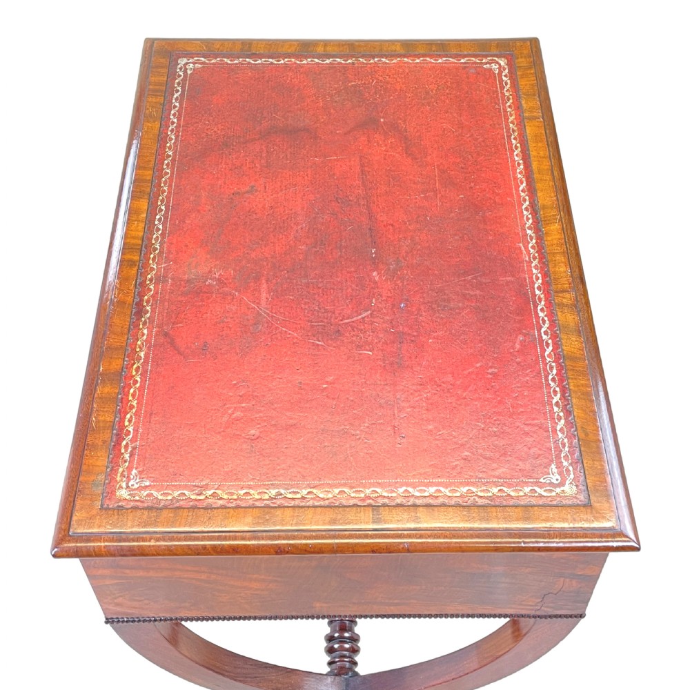 A Regency mahogany writing table featuring a brown leather inset top, two drawers with wooden knobs, curved X-frame legs with a turned stretcher, and brass castors. View V