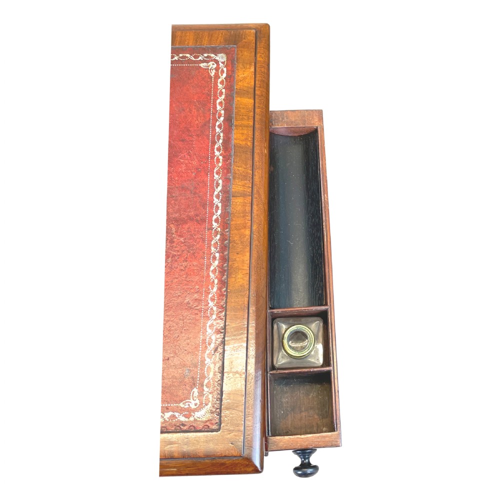 A Regency mahogany writing table featuring a brown leather inset top, two drawers with wooden knobs, curved X-frame legs with a turned stretcher, and brass castors. View VII