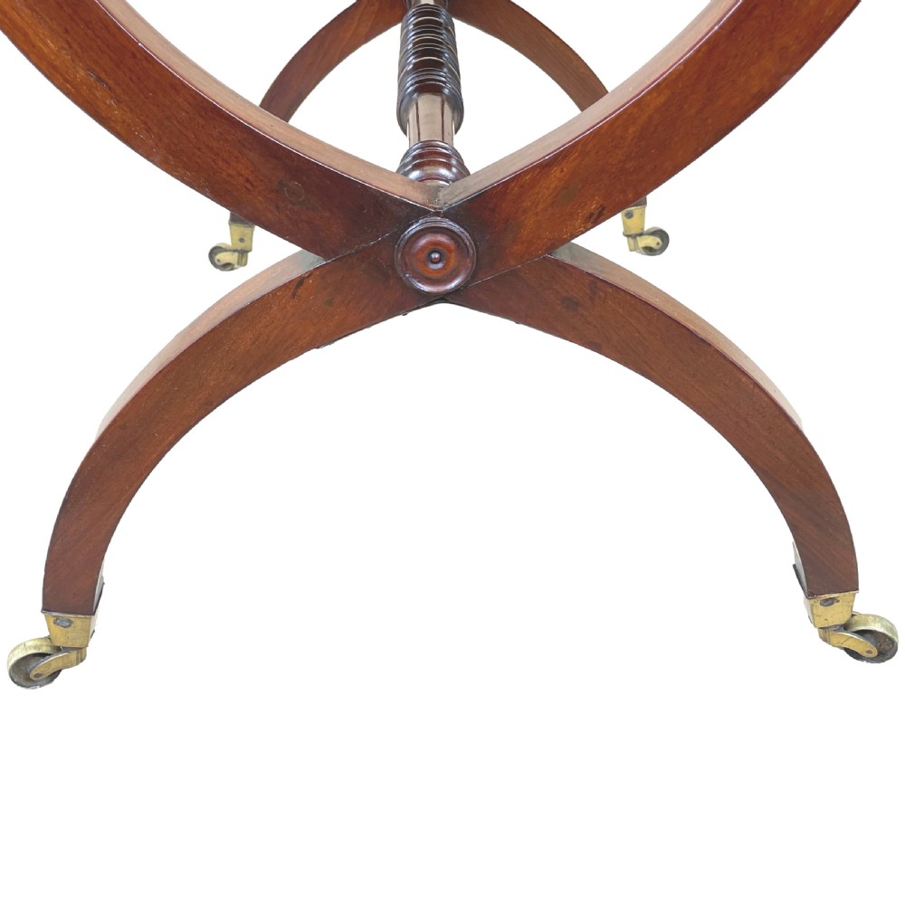 A Regency mahogany writing table featuring a brown leather inset top, two drawers with wooden knobs, curved X-frame legs with a turned stretcher, and brass castors. View IX