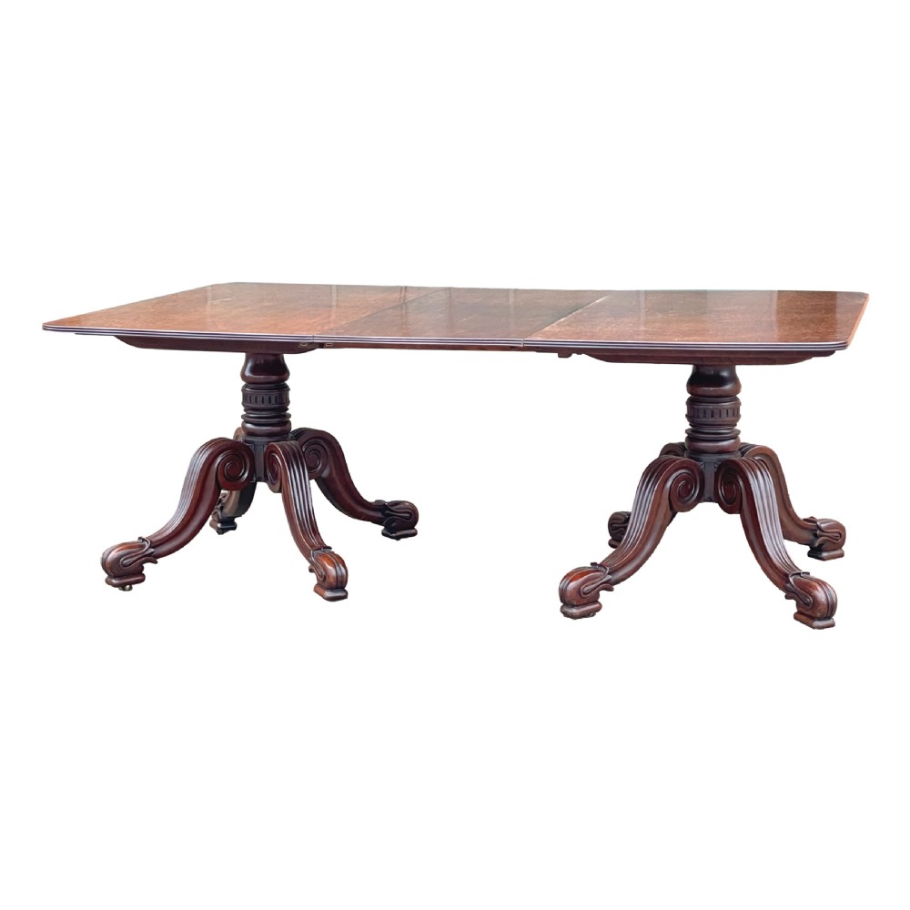 A Regency mahogany twin pillar dining table with an extending centre leaf and carved pedestal supports on brass castors.